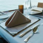 Luxurious dining table setup by the sea with elegant tableware and glassware.