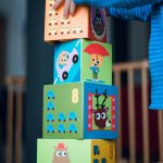 A child playing indoors, stacking colorful wooden toy blocks with joyful illustrations.