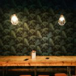 Cozy rustic interior featuring geometric pendant lamps and a large wooden table against a patterned wall.